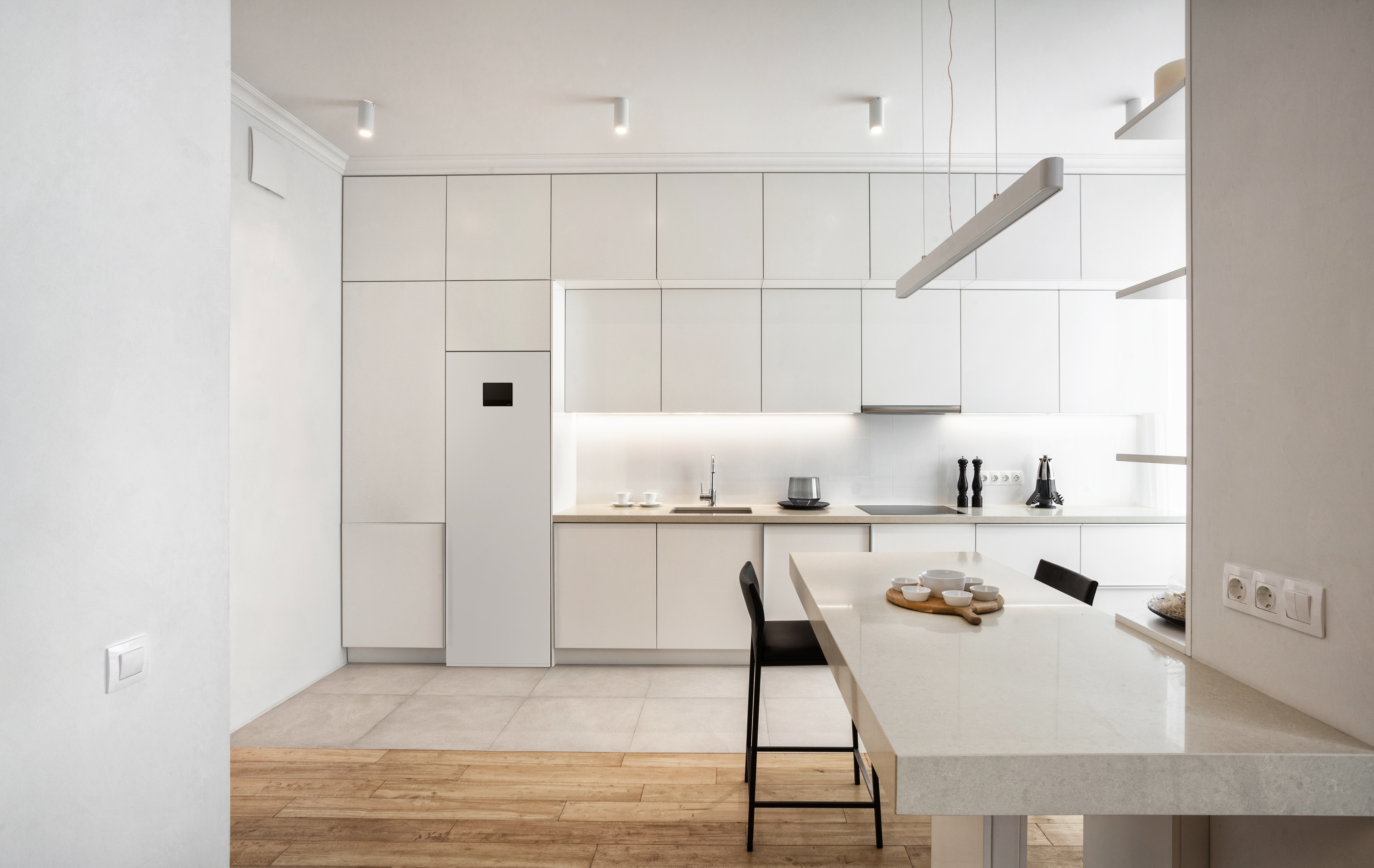Front view of light minimalistic kitchen with white facade, built-in appliances and marble table. Stylish kitchenware on countertop. Well organized space in new apartment